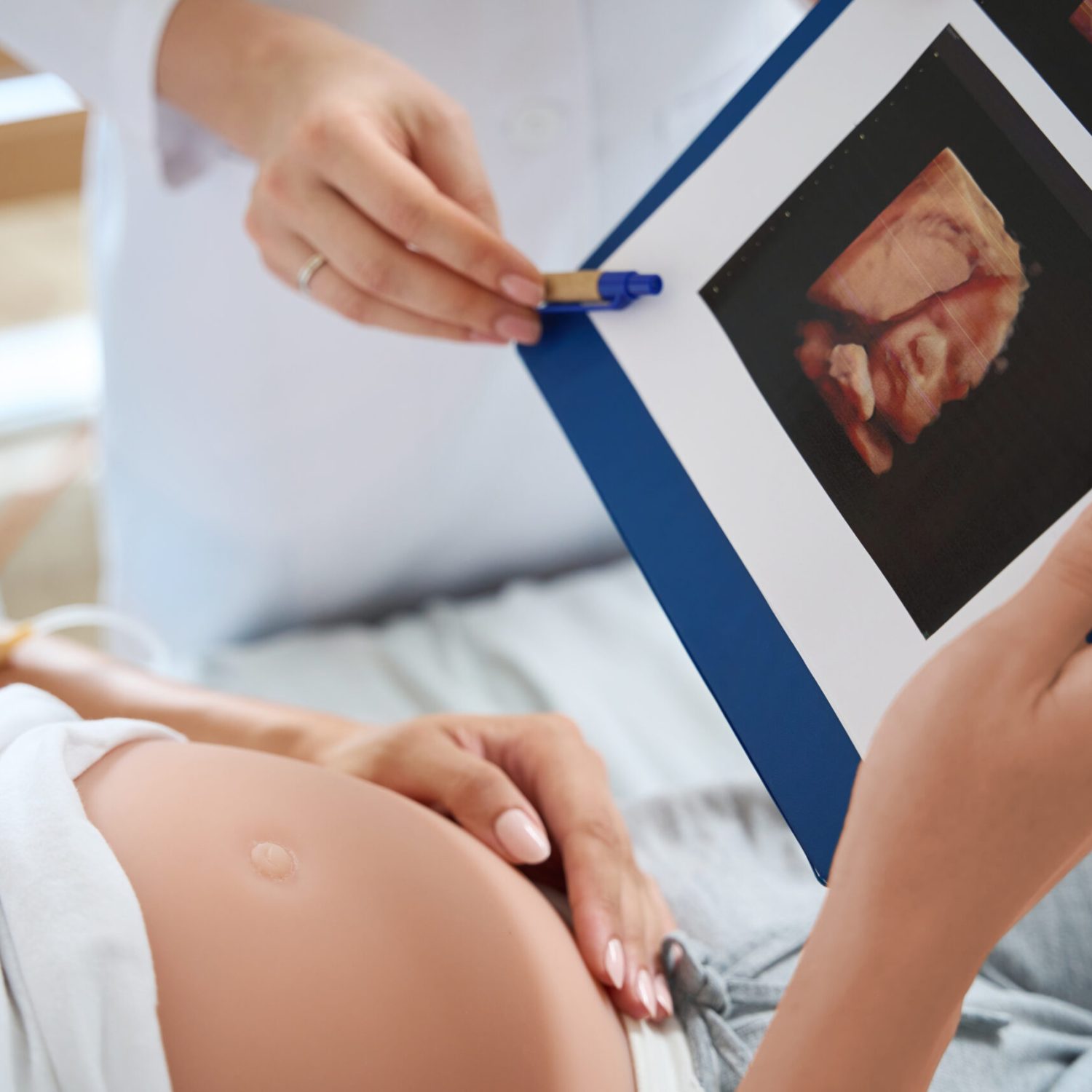 Cropped image of female doctor showing ultrasound photo to pregnant woman on medical bed of her future baby in maternity clinic