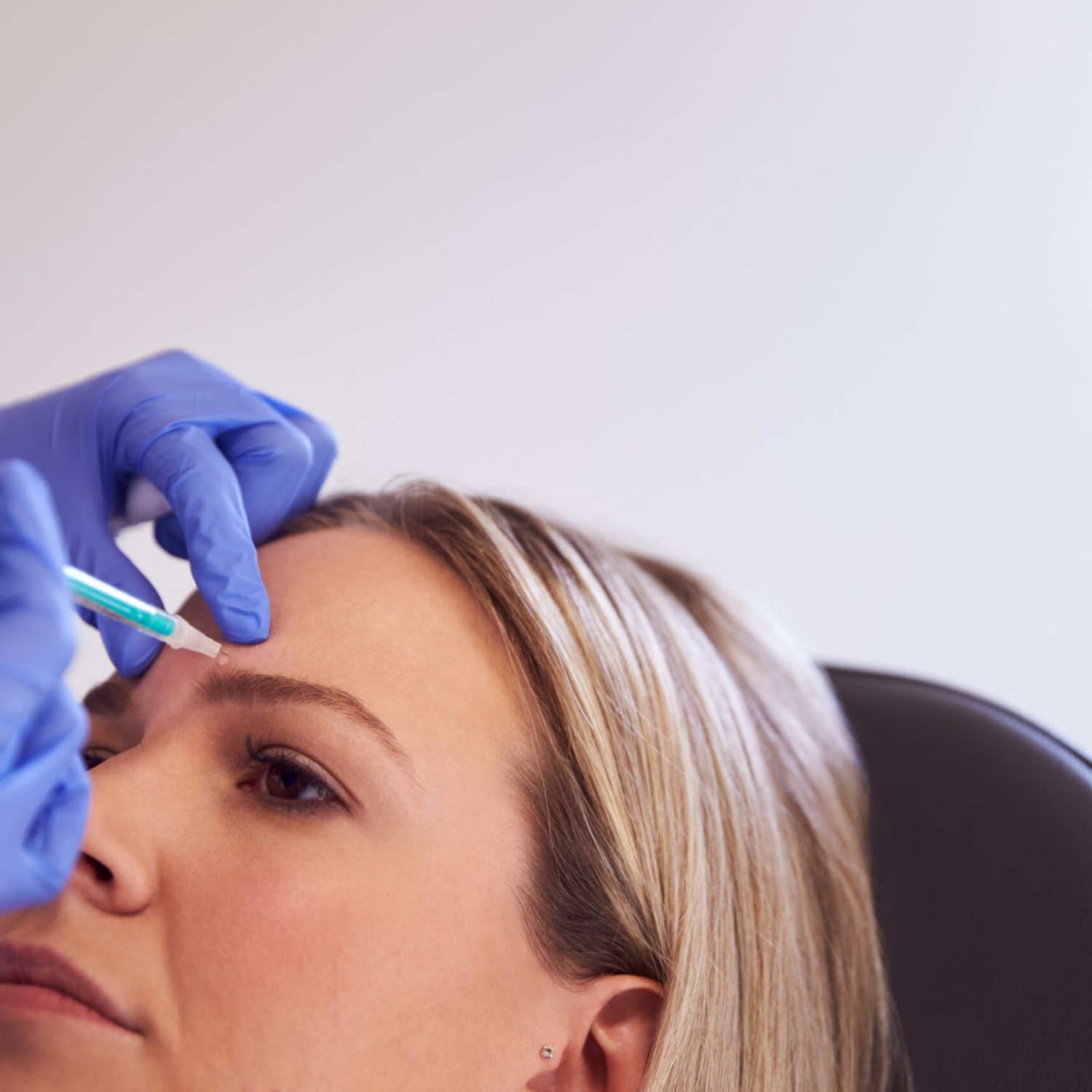 Woman Sitting In Chair Being Give Botox Injection In Forehead By Female Doctor